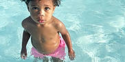 Kynd is registered to the contest to win money with this photo: child, toddler, water, pool, swimming, curly_hair, pink_shorts, summer, outdoor, wet, skin, standing, looking_up, innocent, young, water_ripples, sunlight, playful, vacation, fun