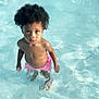 child, toddler, water, pool, swimming, curly_hair, pink_shorts, summer, outdoor, wet, skin, standing, looking_up, innocent, young, water_ripples, sunlight, playful, vacation, fun