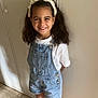 child, girl, smiling, denim_overalls, white_tshirt, headband, indoor, wardrobe, floor, shoes, pink_sneakers, happy, standing, portrait, casual_clothing, hair, young, cute, fashion, person