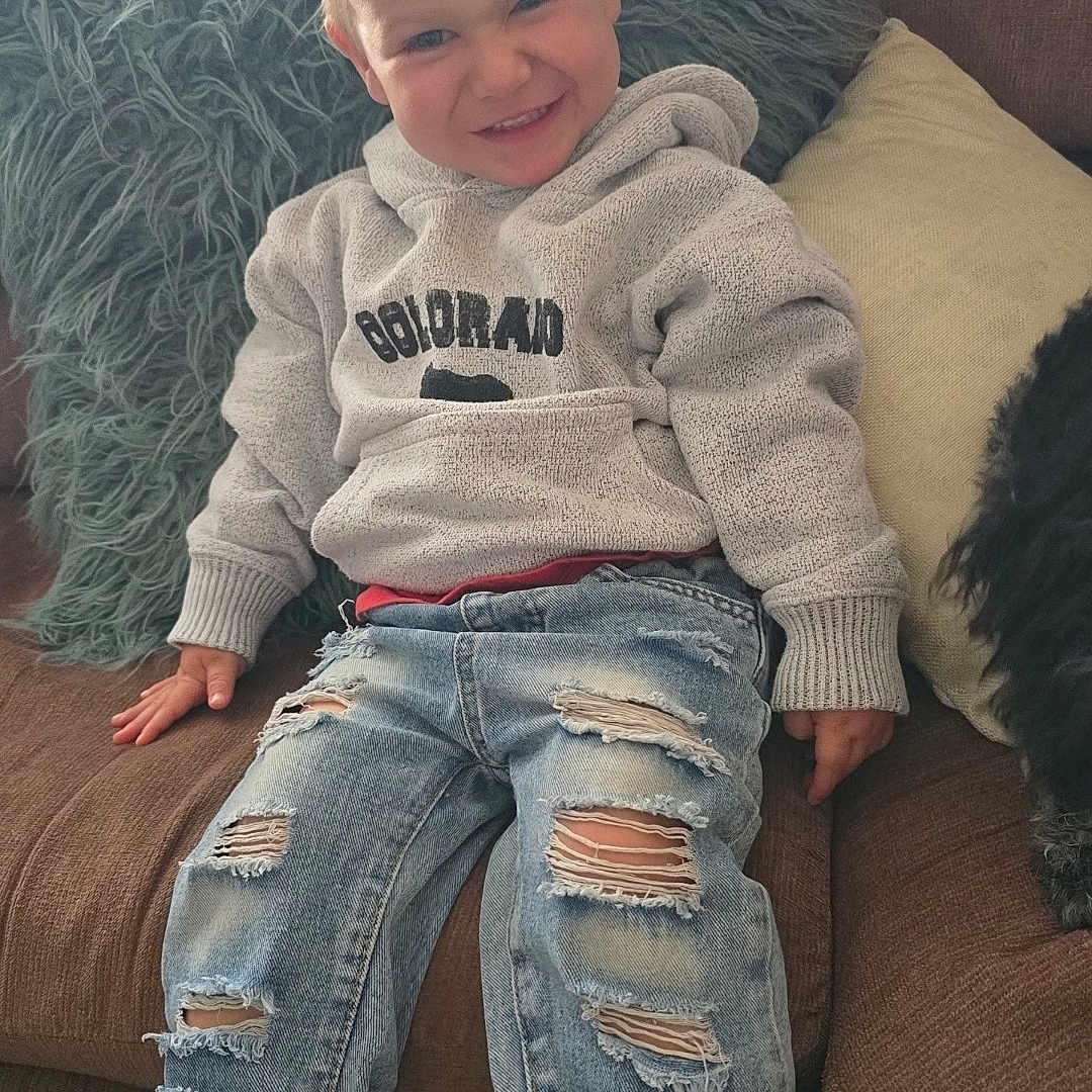 Noah is registered to the contest to win money with this photo: casual_clothing, child, cozy, cushion, cute, fashion, happy, home, hoodie, indoors, person, portrait, relaxed, ripped_jeans, smile, sneakers, sofa, spiky_hair, toddler, youth