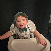 Aiden is registered to the contest to win money with this photo: baby, child, high_chair, smiling, bow_tie, cap, happy, infant, sitting, clothing, face, person, cute, portrait, indoors, furniture, arms_outstretched, baby_fashion, young_child, background