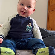Lélio participe au concours pour gagner de l'argent avec cette photo : baby, child, smiling, sitting, socks, sweater, jeans, bed, indoor, cute, face, person, clothing, happy, portrait, young, toddler, room, wooden_furniture, casual