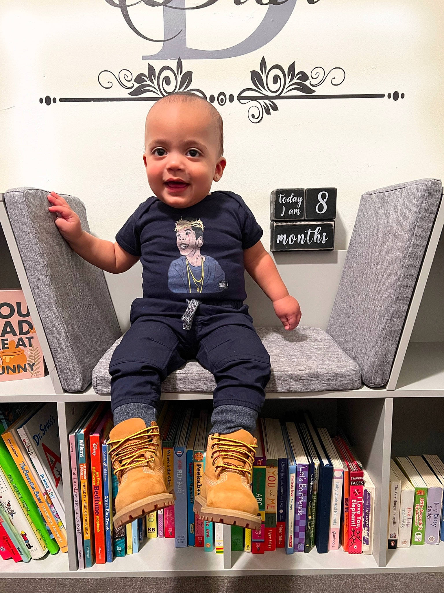 Dior is registered to the contest to win money with this photo: baby, book, bookcase, chair, child, flash_photography, font, gadget, happy, logo, person, product, publication, room, shelf, shelving, sitting, sleeve, smile, t_shirt
