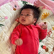 Skyla joined the competition — help win amazing prizes! baby, infant, red_onesie, quilt, floral_pattern, lying_down, curly_hair, indoors, carpet, cute, child, soft_texture, patterned_blanket, small_hands, portrait, young_child, relaxed, cozy, colorful, playful