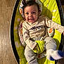 baby, child, smiling, happy, infant, baby_rocker, clothing, socks, floor, wooden_floor, head, face, seat, cushion, toy, indoor, person, playful, cute, young