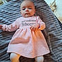 baby, blanket, child, cozy, cute, expressionless, face, floor, home_interior, indoors, infant, lying_down, person, pink_dress, portrait, soft_texture, text_on_clothing, toddler, white_tights, young_child