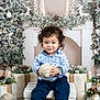 Jaxon joined the competition — help win amazing prizes! toddler, child, curly_hair, blue_shirt, navy_pants, holiday_decor, christmas, ornament, pine_branches, wrapped_gifts, white_bench, festive, smile, indoor, seasonal, decorations, reindeer, winter, cute, portrait