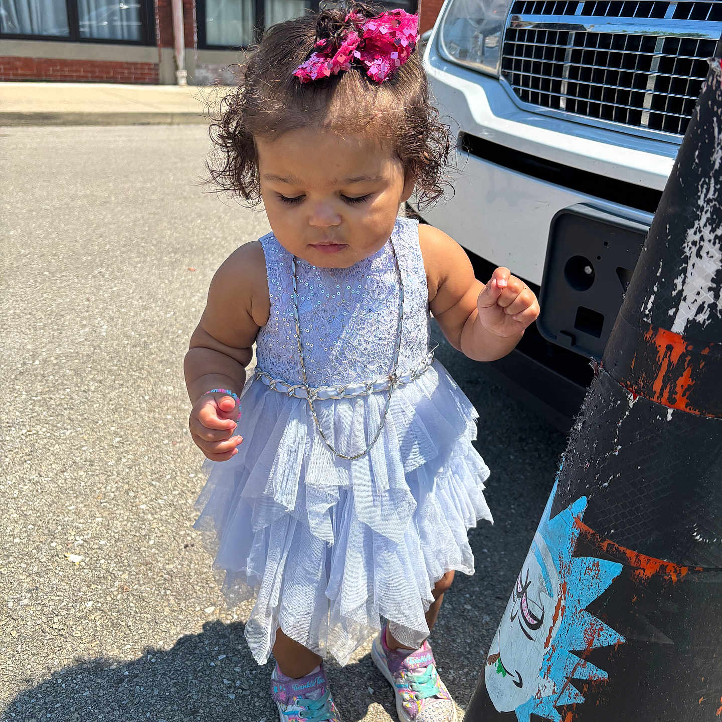 Kiayeh joined the competition — help win amazing prizes! building, child, concrete, curly_hair, daylight, dress, necklace, outdoor, pavement, pink_bow, shadow, sneakers, sticker, sunny, toddler, toy, traffic_cone, vehicle, window, yellow_block