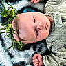 baby, sleeping, blanket, green_clothing, leaf_crown, infant, peaceful, soft_texture, patterned_blanket, cute, resting, indoors, portrait, child, hands, small_fingers, head, natural_elements, cozy, relaxed