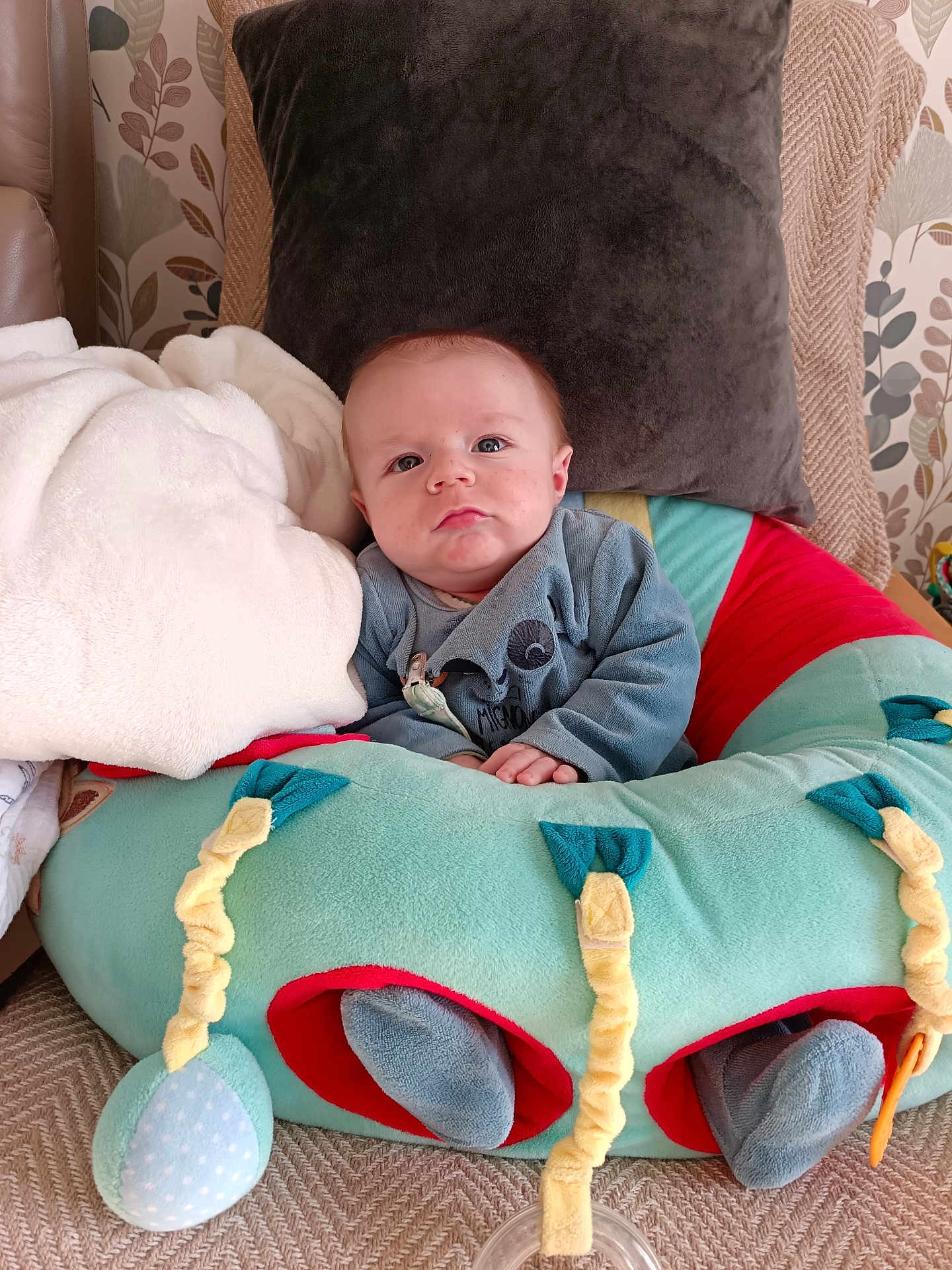 Thélio a rejoint le concours — aidez-le/la à gagner de superbes lots ! baby, infant, plush_cushion, blanket, pillow, face, clothing, indoors, seated, cozy, soft_toy, cute, child, living_room, home_decor, person, blue_eyes, expression, comfort, small_hands