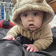 Briar is registered to the contest to win money with this photo: baby, child, hoodie, fluffy_clothing, cute, indoors, crawling, wide_eyes, curious, soft_texture, plaid_blanket, black_surface, hand, face, person, warm_clothing, infant, cozy, expression, closeup