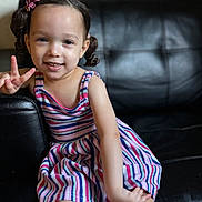 Winter joined the competition — help win amazing prizes! child, girl, smiling, peace_sign, striped_dress, pigtails, hair_bows, sitting, couch, leather, indoor, portrait, happy, cute, young_child, person, casual, fashion, playful, colorful