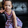 child, girl, smiling, peace_sign, striped_dress, pigtails, hair_bows, sitting, couch, leather, indoor, portrait, happy, cute, young_child, person, casual, fashion, playful, colorful