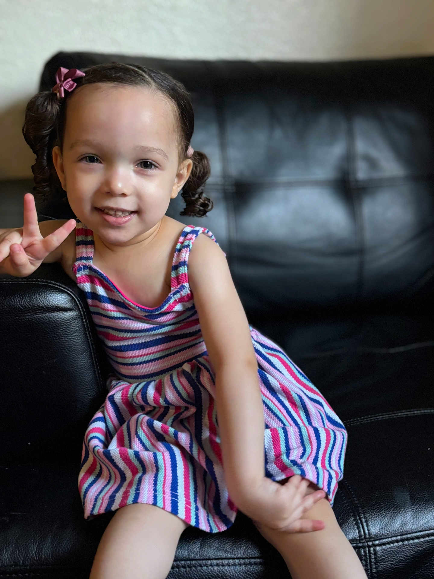 Winter joined the competition — help win amazing prizes! child, girl, smiling, peace_sign, striped_dress, pigtails, hair_bows, sitting, couch, leather, indoor, portrait, happy, cute, young_child, person, casual, fashion, playful, colorful