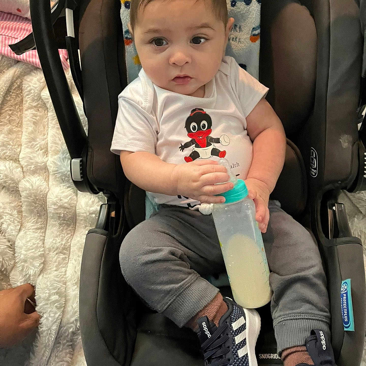 Jeesterd joined the competition — help win amazing prizes! adidas, baby, blanket, bottle, car_seat, clothing, fabric, face, footwear, gray_pants, hand, indoor, milk, person, sitting, sneakers, toddler, toy, white_shirt, young_child