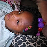Va'Neyia is registered to the contest to win money with this photo: beads, black_hair, braids, casual, child, closeup, colorful, comfort, face, head, indoor, looking, pattern, person, pillow, portrait, relaxed, resting, sweatshirt, young