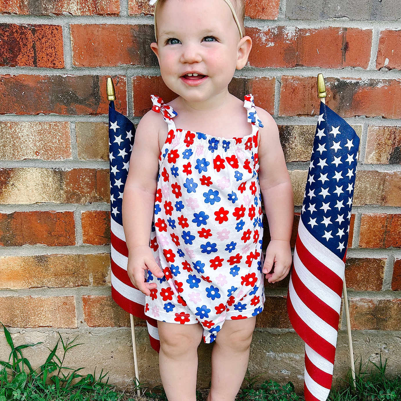 Millie joined the competition — help win amazing prizes! american_flag, baby, barefoot, brick_wall, celebration, child, colorful, cute, flag, flower_pattern, grass, happy, headband, outdoor, person, portrait, romper, smiling, summer, toddler