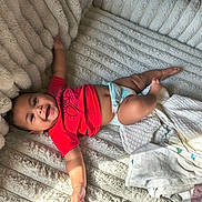 Kash is registered to the contest to win money with this photo: baby, infant, smiling, red_shirt, diaper, blanket, soft_texture, cozy, lying_down, happy, child, cute, plush, comfort, indoor, person, toddler, reaching, skin, head