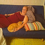 Chrystal participe au concours pour gagner de l'argent avec cette photo : adult, blanket, blue_sofa, casual, cat, comfort, glasses, home, indoor, maroon_dress, orange_cat, pet, pillow, relaxed, remote_control, resting, sofa, striped_pillow, tile_floor, woman