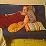 adult, blanket, blue_sofa, casual, cat, comfort, glasses, home, indoor, maroon_dress, orange_cat, pet, pillow, relaxed, remote_control, resting, sofa, striped_pillow, tile_floor, woman