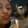Kiki is registered to the contest to win money with this photo: animal, bed, cat, close_up, clothing, cozy, curious, face, floor, fur, head, home, indoor, interaction, looking, person, pet, puckered_lips, siamese_cat, whiskers