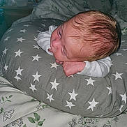 Danté is registered to the contest to win money with this photo: baby, infant, pillow, star_pattern, bed, blanket, floral, sleeping, resting, indoors, person, skin, hair, hand, face, clothing, white_sleeve, cute, newborn, cozy