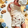 baby, infant, child, portrait, lying_down, smiling, bunny_hat, white_clothing, patterned_shorts, wooden_toys, toy_cars, balloons, fairy_lights, flowers, blue_flowers, gold_balloons, nursery, celebration, indoor, cute