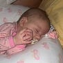 baby, sleeping, pajamas, pink, hand, face, pillow, butterfly_pattern, yellow_pillow, infant, peaceful, closeup, soft_lighting, child, cute, resting, indoors, person, newborn, calm