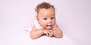 Jasmine joined the competition — help win amazing prizes! baby, curly_hair, tongue_out, pink_background, infant, cute, playful, child, portrait, smiling, lying_down, soft_texture, light_skin, wearing_clothes, hands_together, indoors, bright, closeup, head_and_shoulders, adorable