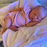 Nevaeh is registered to the contest to win money with this photo: baby, sleeping, pink_outfit, blanket, cushion, infant, newborn, soft_texture, cozy, peaceful, indoor, resting, child, cute, small, human, portrait, bedroom, comfort, relaxation