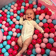 Lottie is registered to the contest to win money with this photo: baby, ball_pit, balls, pink, red, blue, tent, unicorn, smile, happy, infant, child, play, colorful, cute, onesie, indoors, toy, fun, joyful