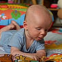 Erik is registered to the contest to win money with this photo: baby, infant, child, blue_onesie, fabric_book, colorful, play_area, toy, lying_down, tummy_time, curious, indoor, soft_light, patterned_blanket, close_up, face, hand, skin, head, expression
