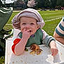 baby, child, toddler, highchair, hat, bib, bread_roll, eating, smiling, crumbs, hand, outdoor, park, grass, stroller, picnic, sunlight, portrait, headwear, happy