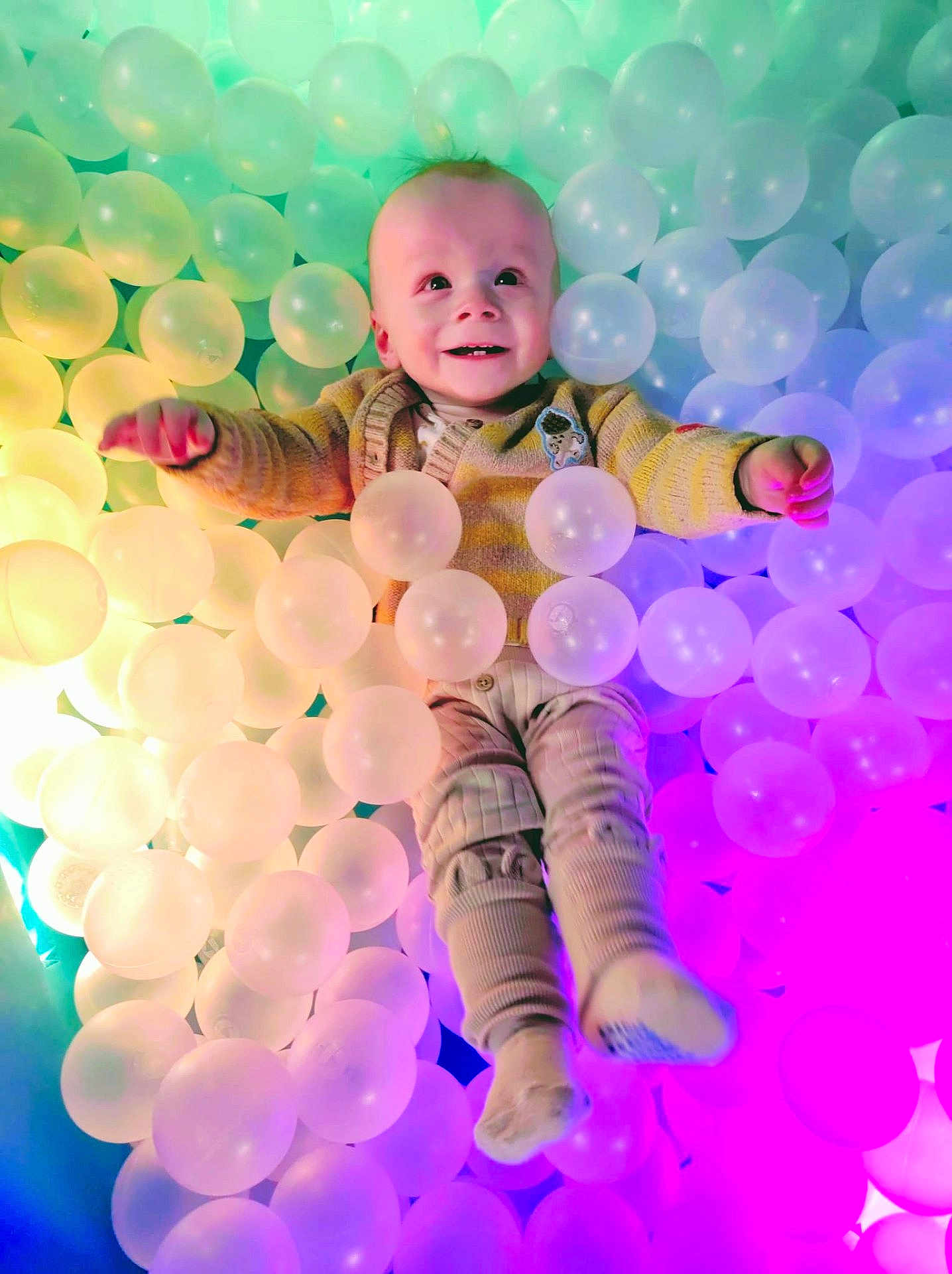 Erik joined the competition — help win amazing prizes! baby, infant, smile, ball_pit, plastic_balls, colorful, pastel, rainbow_lighting, sweater, socks, play, joyful, portrait, top_view, looking_up, face, eyes, hands, legs, soft_texture