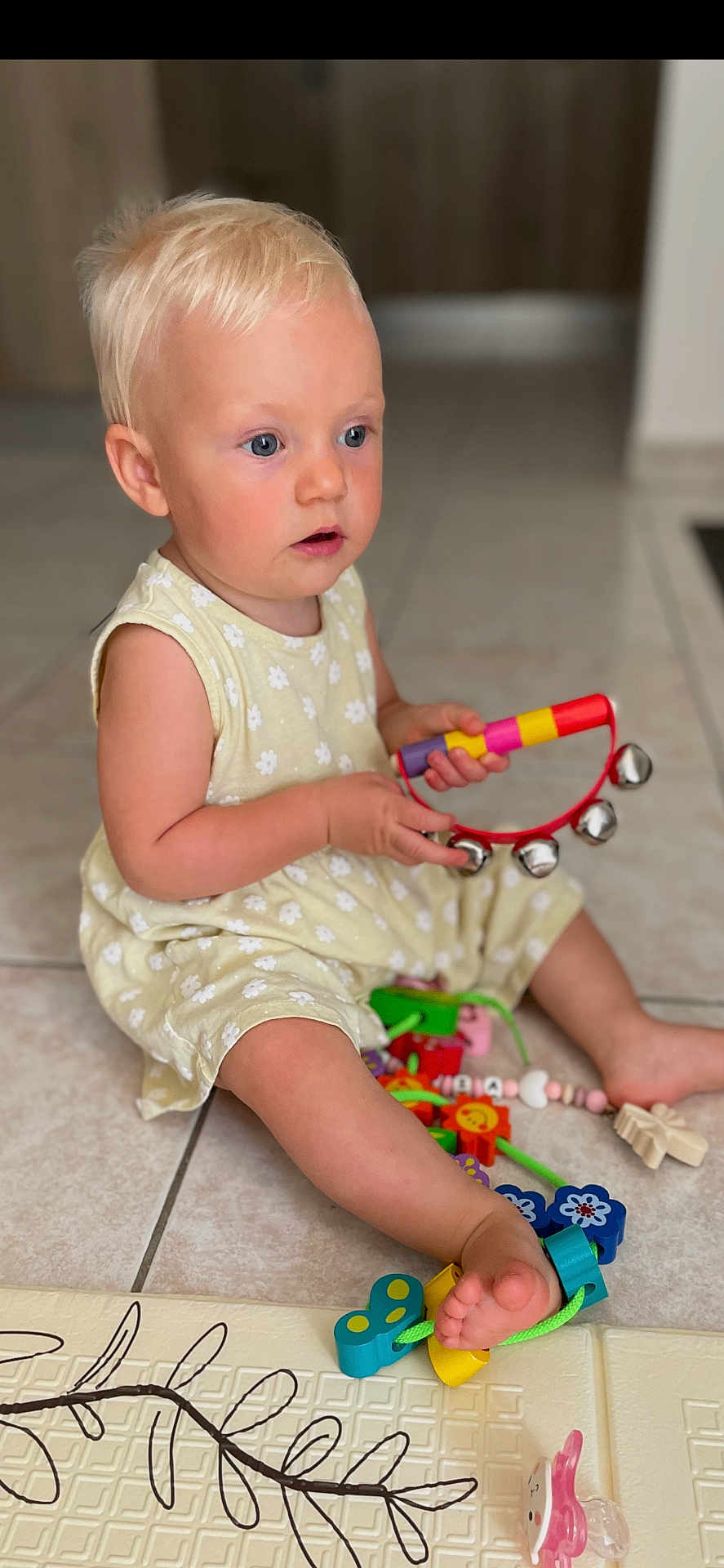 Victoria Grorod participe au concours pour gagner de l'argent avec cette photo : toddler, child, blonde_hair, blue_eyes, yellow_dress, sitting, floor, tiles, tambourine, toy, colorful, indoor, pacifier, foot, play, curious, young_child, person, baby, cute