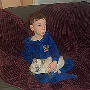 Tiago a rejoint le concours — aidez-le/la à gagner de superbes lots ! child, boy, cat, siamese_cat, onesie, blue_clothing, plush_blanket, maroon_blanket, couch, indoor, pet, animal, sitting, relaxed, home, cozy, furniture, portrait, young, companion