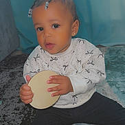 Taliyah is registered to the contest to win money with this photo: toddler, child, baby, indoor, carpet, sitting, holding_object, sweater, black_pants, braided_hair, beads, earring, curtain, blue, patterned_carpet, cute, portrait, person, floor, soft_light