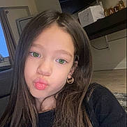 Emeri is registered to the contest to win money with this photo: child, girl, green_eyes, long_hair, pouting, selfie, earrings, black_top, indoor, living_room, furniture, decor, shelf, fall_decoration, portrait, cute, young, face, person, casual