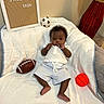 baby, basketball, blanket, celebration, child, cute, decor, football, happy, home, indoor, infant, letter_board, lying_down, milestone, portrait, smiling, soccer_ball, sports_ball, white_clothing