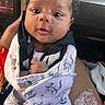 baby, infant, child, blanket, dinosaur_pattern, clothing, hand, car_interior, seat, person, face, cute, young, wrapped, portrait, newborn, small_hands, expression, indoor, cozy