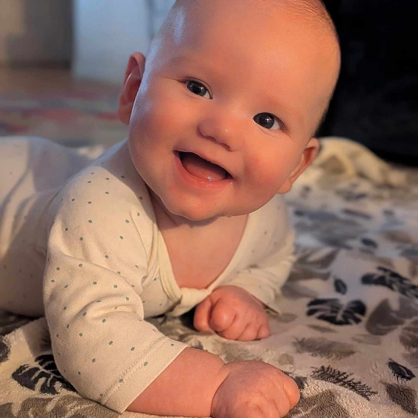 Brendan is registered to the contest to win money with this photo: baby, child, infant, smiling, happy, portrait, crawling, sitting, indoors, bedroom, bed, blanket, bedspread, onesie, clothing, face, eyes, hands, warm_lighting, adorable