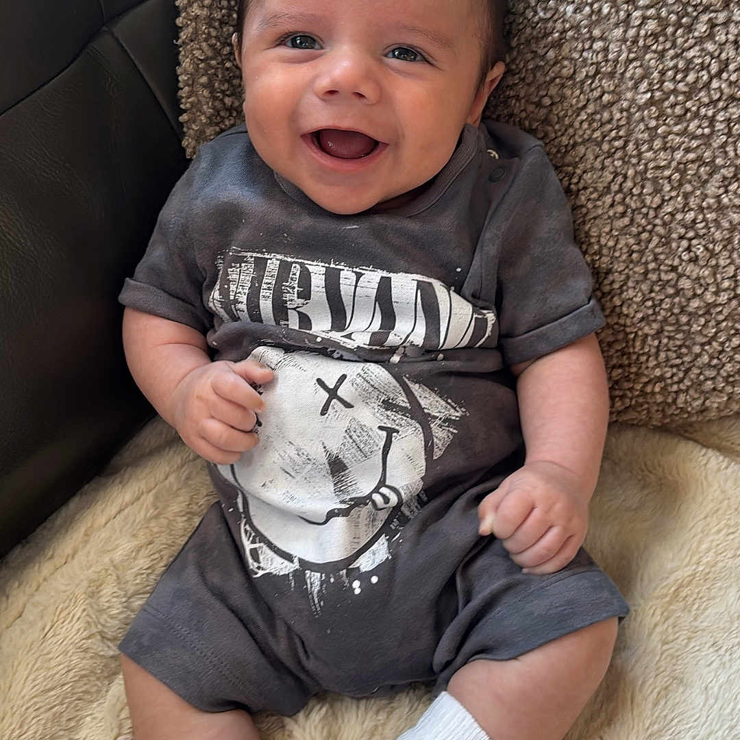 Kasen is registered to the contest to win money with this photo: baby, blanket, child, clothing, couch, cozy, cute, face, happy, indoor, infant, person, pillow, portrait, shoes, sitting, smiling, sneakers, socks, tshirt