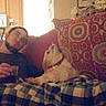 beard, blanket, brown_dog, casual, couch, cozy, dog, furniture, home, indoor, living_room, looking_up, man, patterned, pet, pillow, plaid, plush, relaxing, seated