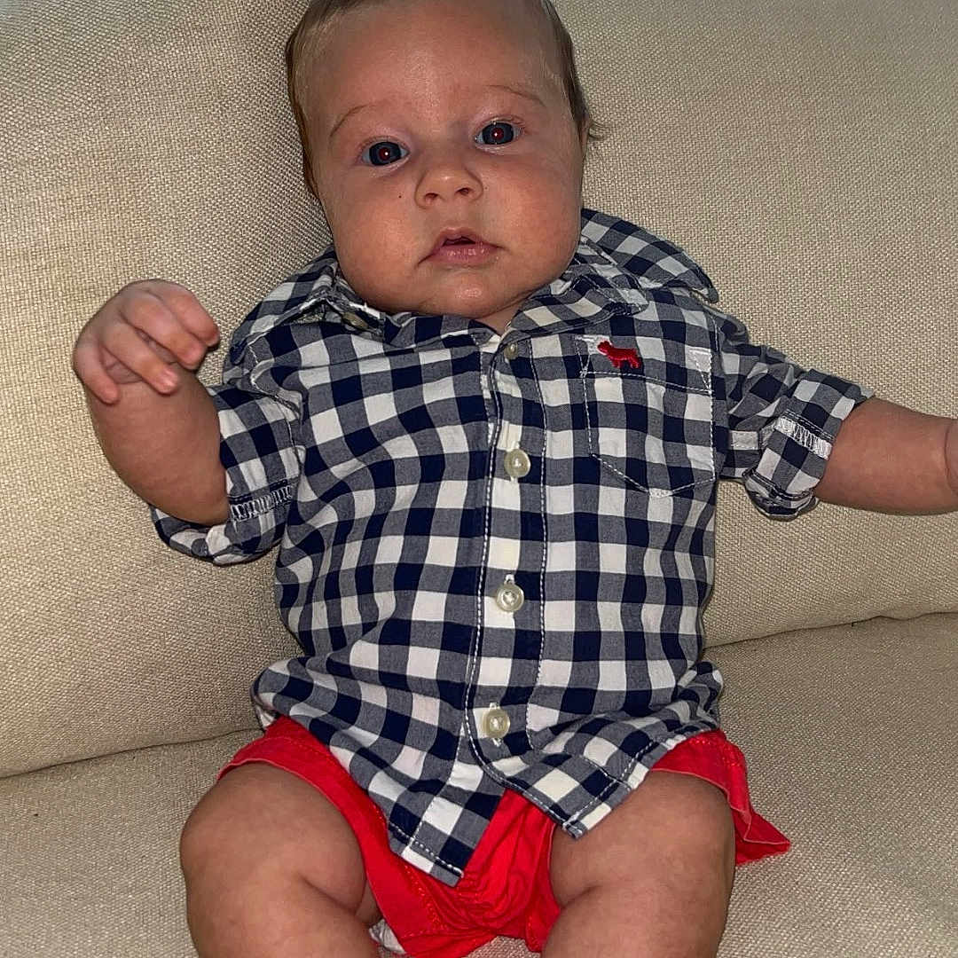 Kollins is registered to the contest to win money with this photo: baby, barefoot, child, clothing, couch, curtain, expression, face, feet, furniture, home, indoor, infant, portrait, seated, shirt, shorts, skin, window, young