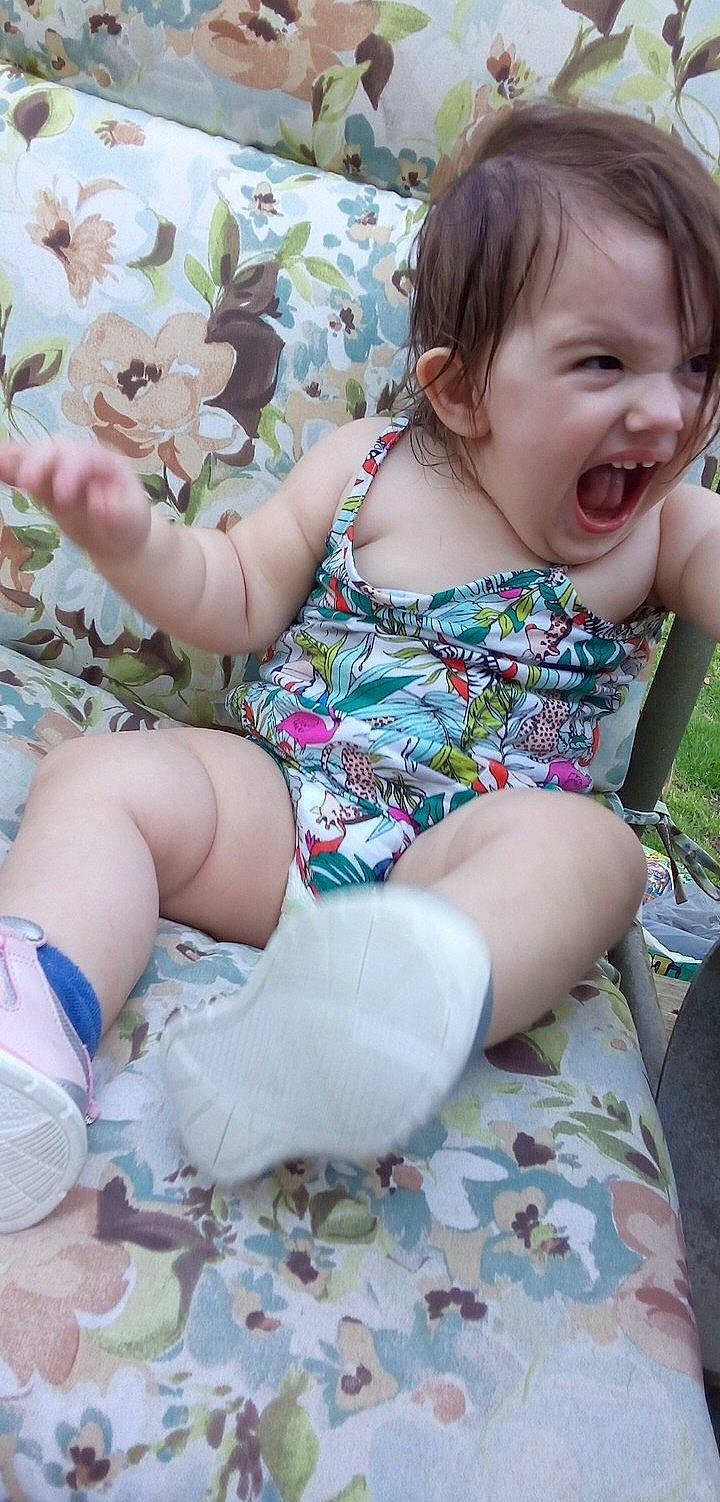 Natalie is registered to the contest to win money with this photo: baby_toddler_clothing, child, clothing, face, finger, grass, hairstyle, happy, head, human_leg, knee, lap, leg, person, pink, skin, sleeve, smile, sock, thigh