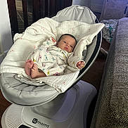 Elena is registered to the contest to win money with this photo: baby, infant, blanket, butterfly_print, baby_rocker, swaddled, face, indoor, wooden_floor, furniture, cushion, clothing, person, newborn, resting, cute, home, soft, peaceful, gazing