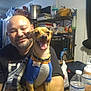 man, dog, smiling, pet, indoor, table, water_bottle, sweater, kitchen, sitting, happy, person, face, bald, beard, shelf, container, plastic_bag, blanket, collar