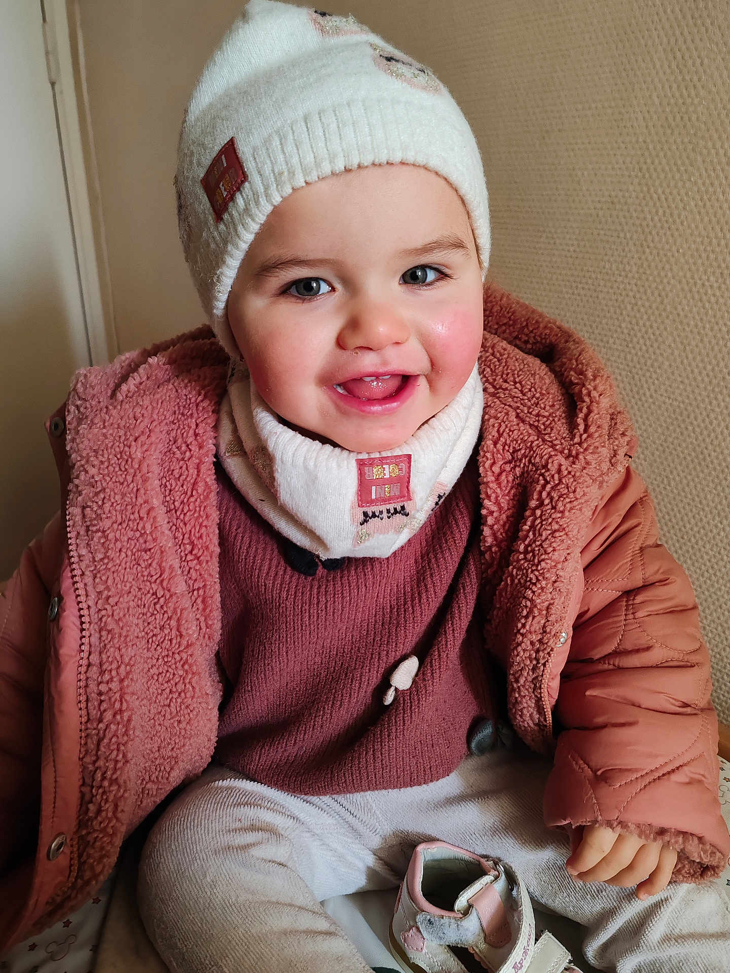 Mélina participe au concours pour gagner de l'argent avec cette photo : child, toddler, beanie, hat, pink_coat, scarf, smile, rosy_cheeks, teeth, sitting, shoe, hand, indoor, portrait, cozy, winter_clothes, cute, jacket, face, happy