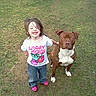 child, dog, grass, outdoor, happy, smiling, casual_clothing, tshirt, jeans, pink_shoes, pet, animal, friendship, playful, nature, daylight, young, cute, fun, portrait