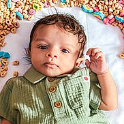 Davion is registered to the contest to win money with this photo: baby, infant, child, newborn, portrait, face, eyes, hand, green_shirt, buttons, lying_down, white_blanket, breakfast_cereal, cereal_loops, colorful_marshmallows, cute, soft_texture, closeup, hair, playful_setup